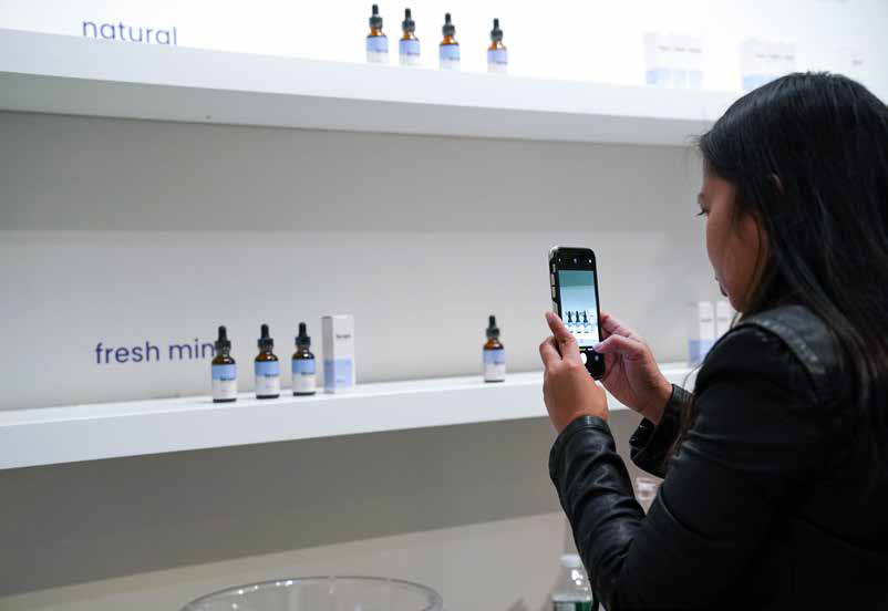 Shopper photographing a skincare shelf during A Day Well Spent, Naked Retail engagement and acquisition by SheridanCX